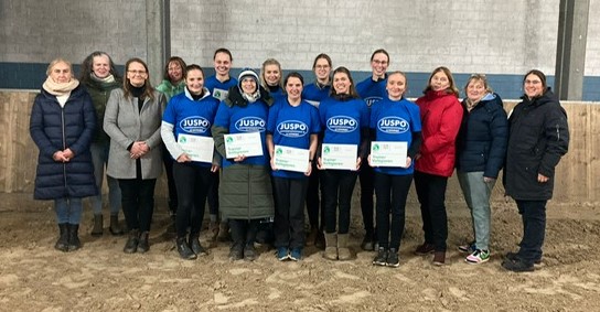 Auf dem Foto strahlen 9 Teilnehmerinnen nach der erfolgreichen Abschluss-Prüfung mit dem Lehrgangsteam um die Wette, sie tragen dabei die blauen JUSPO-Shirts